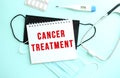 The red text CANCER TREATMENT is written on a notepad that sits on a blue background next to medical supplies.