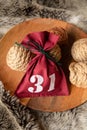 Red textile bag tied with green thread with date number thirty one, twine and natural rope coils on wooden round tray on faux fur Royalty Free Stock Photo