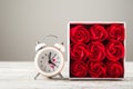 Red textured roses and alarm clock close-up and copy space. Women`s day, mother`s day, red roses and a clock on a white wooden bac Royalty Free Stock Photo