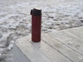Red thermocup on a white wooden table against the background of white snow in the chilly weather