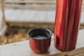 Red thermos bottle with cup in wooden house on background of wwoden trail. Close up.