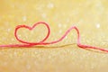 Red thread in the shape of a symbol of love of heart on a gold background for Valentine`s day Royalty Free Stock Photo