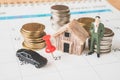 Red thumbtack on calendar with miniature businessman , blurred car, stack of coins and small house Royalty Free Stock Photo