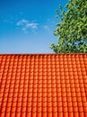 Red tiled roof. CLouds in blue sky. Green tree. Spring or summer nature.