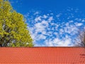 Red tiled roof. CLouds in blue sky. Green tree. Spring or summer nature.