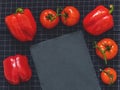 Red tomatoes on a branch, red pepper, cutting board slate on black cloth background with blank space for text. Flat lay. Top view