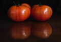 Red tomatoes on a dark wooden surface where are reflected