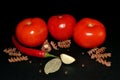 Red tomatoes and red hot pepper, garlic, bay leaf, pasta on black background Royalty Free Stock Photo