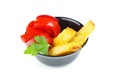 Red tomatoes and polenta pieces in black ceramic bowl. Isolated on white