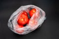 Red tomatoes in transparent open plastic bag on grey background.