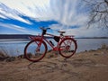 Red tourist bike by the river on a background of blue cloudy sky on a sunny spring day