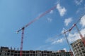 Red tower cranes on construction site unfurling their arrows over upper floors of gray frames of residential apartment buildings