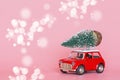 Red toy car with a christmas tree on the roof on pink paper background. Winter delivery, xmas, happy new year 2020 celebration Royalty Free Stock Photo