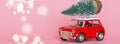 Red toy car with a christmas tree on the roof on pink paper background. Winter delivery, xmas, happy new year 2020 celebration Royalty Free Stock Photo