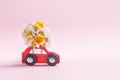 Red toy car delivering beautiful bouquet of wild flowers on pink background. Flower delivery conncept