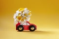 Red toy car delivering bouquet of flowers box on yellow background. Flower delivery. Happy Women`s Day conncept