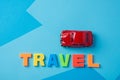 Red toy car and inscription plastic travel letters on a blue background