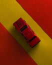 A red toy car is isolated in yellow background surrounded by red border