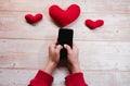 Red toy hearts on wooden table. Hold smartphone in hands and write message, congratulate someone on Valentines day on February 14