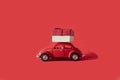 Red toy retro car delivering a gift on a red background. Postcard for the new year, Christmas, Valentine`s Day. Delivery of gifts Royalty Free Stock Photo
