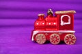 Red toy train locomotive on a purple and lilac gradient background. New Year or Christmas card. Icicles and snow on a Royalty Free Stock Photo