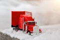 Red toy truck rides on a winter snowy road. Wood flooring. Front view, close-up of a cargo tractor