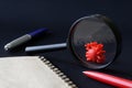 Red toy virus under a magnifying glass on a black background next to a notebook and pen. The concept of studying new viruses, Royalty Free Stock Photo