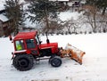 A red tractor clears the road from the snow. Winter cleaning of the street. Community service. Weather. Winter village. Snowblower Royalty Free Stock Photo