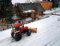 A red tractor clears the road from the snow. Winter cleaning of the street. Community service. Weather. Winter village. Snowblower Royalty Free Stock Photo