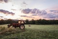 Red tractor and freshly rolled hay bales rest on rolling hill with dramatic cloudscape at sunrise Royalty Free Stock Photo