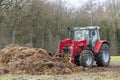 Red tractor with front loader in front of a manure heap Royalty Free Stock Photo