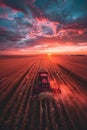 A red tractor harvests corn in a field at sunset, with the setting sun casting an orange glow over the landscape Royalty Free Stock Photo