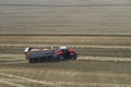 A red tractor harvests ripe golden wheat on a grain field harvested by harvesters. Agricultural work in summer. Royalty Free Stock Photo