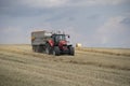 A red tractor harvests ripe golden wheat on a grain field harvested by harvesters. Agricultural work in summer. Royalty Free Stock Photo