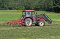 Red tractor with a hay rake machine at work on a field Royalty Free Stock Photo