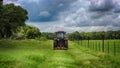 Red tractor mowing grass under rainy sky Royalty Free Stock Photo