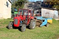 Red tractor parked next to family house with old agricultural equipment in background surrounded with barn and other tractor in Royalty Free Stock Photo