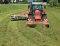 Red tractor with a rotary disc mower cutting the grass of a fallow field