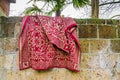 Red traditional persian carpet hanging outside over a stone wall