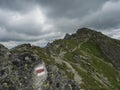 Red trail post sign at steep hiking path on ridge of rohace mountain to peak ostry rohac. Sharp green rocks, Summer blue