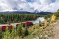 Red train long freight on railway passing in autumn valley and bow river at Morant's Curve Royalty Free Stock Photo