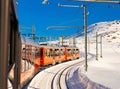 Red train running on rack railway through snowy Swiss Alps