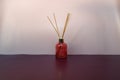 Red transparent glass aroma diffuser with five wooden sticks on purple color background