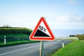 Red triangle road sign indicating a steep 10 percent downhill gradient in the road ahead. Empty road with crash barriers