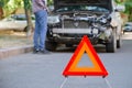 Red triangle warning sign of car accident on road in front of wrecked car. Man inspecting wrecked car after accident Royalty Free Stock Photo