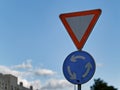 A red triangle yield or give way roundabout sign attached on a pole against a blue sky Royalty Free Stock Photo