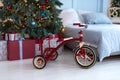 Red tricycle bike with Xmas gift at room. Bright bedroom with decorated christmas tree and comfortable bed. Royalty Free Stock Photo