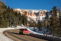 Red truck driving up winding canyon road toward desert towers of red sandstone