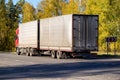A red truck with a semi-trailer transports goods along a country highway against the backdrop of an autumn forest. Tonnage per