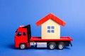 Red truck transports a red roofed house. Concept of transportation and cargo shipping, moving company. Construction of new houses